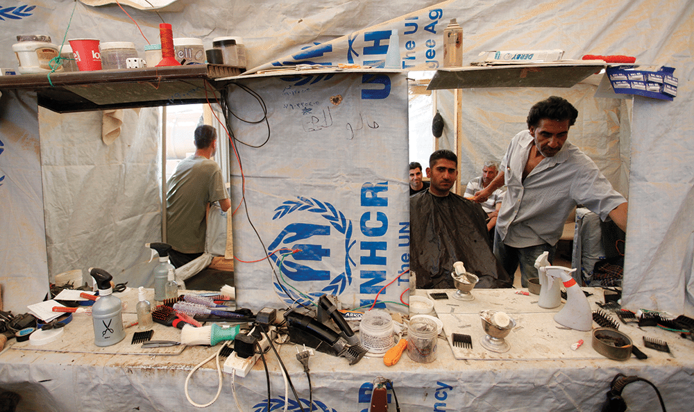 Abd al-Raouf Abo Majd, 45, right, known as 'the Zaatari barber', cuts a Syrian refugee's hair in his UNHCR tent barbershop, at Zaatari refugee camp on 25th April 2013. Photo: Mohammad Hannon/AP/Press Association Images