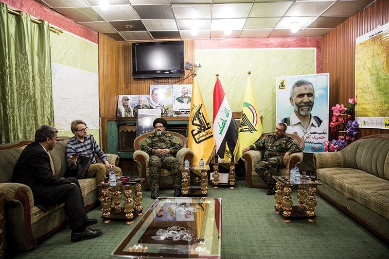 Commander Ali al-Yaseri of Saraya al-Khorasani (far right) is accompanied by deputy commander Hamid al-Jazaeiri for our interview. Pictures of Iranian generals including Hamid Taghavi (large poster on right) and Qassem Suleimani adorn the walls