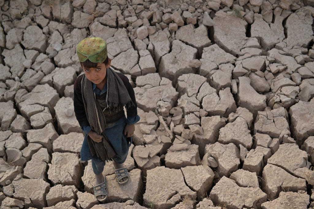 Boy stands in extreme drought, dried cracked earth.