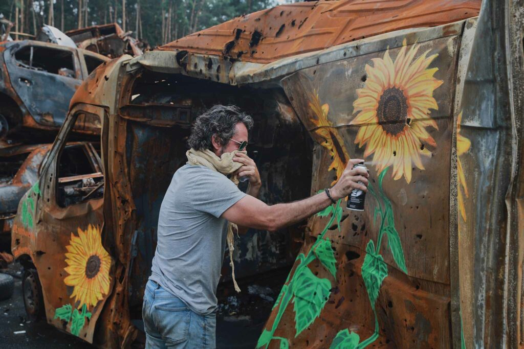 An artist spraypaints sunflowers, a symbol of Ukraine, on a burnt-out, bullet-riddled van