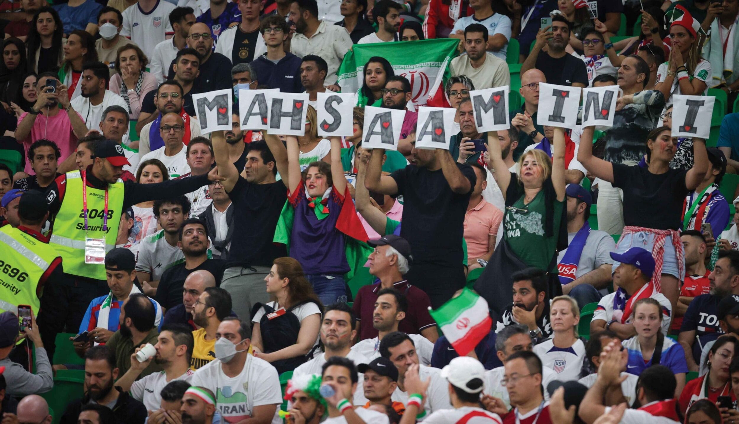 Security guards approach supporters, including Arman Jabbari, holding letters forming the name Mahsa Amini at the Iran vs US game, 29th November 2022 
